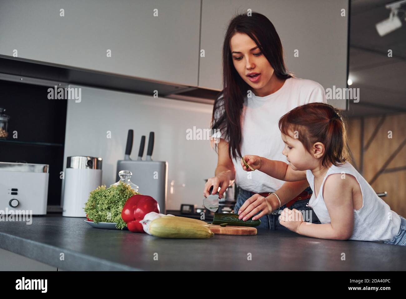 Madre con la figlia piccola che affetta le verdure all'interno in cucina Foto Stock