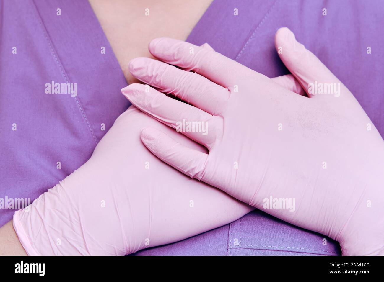 Concetto di soggiorno a casa, mani piegate sul cuore. Medico in guanti protettivi e uniforme medica, primo piano. Foto Stock