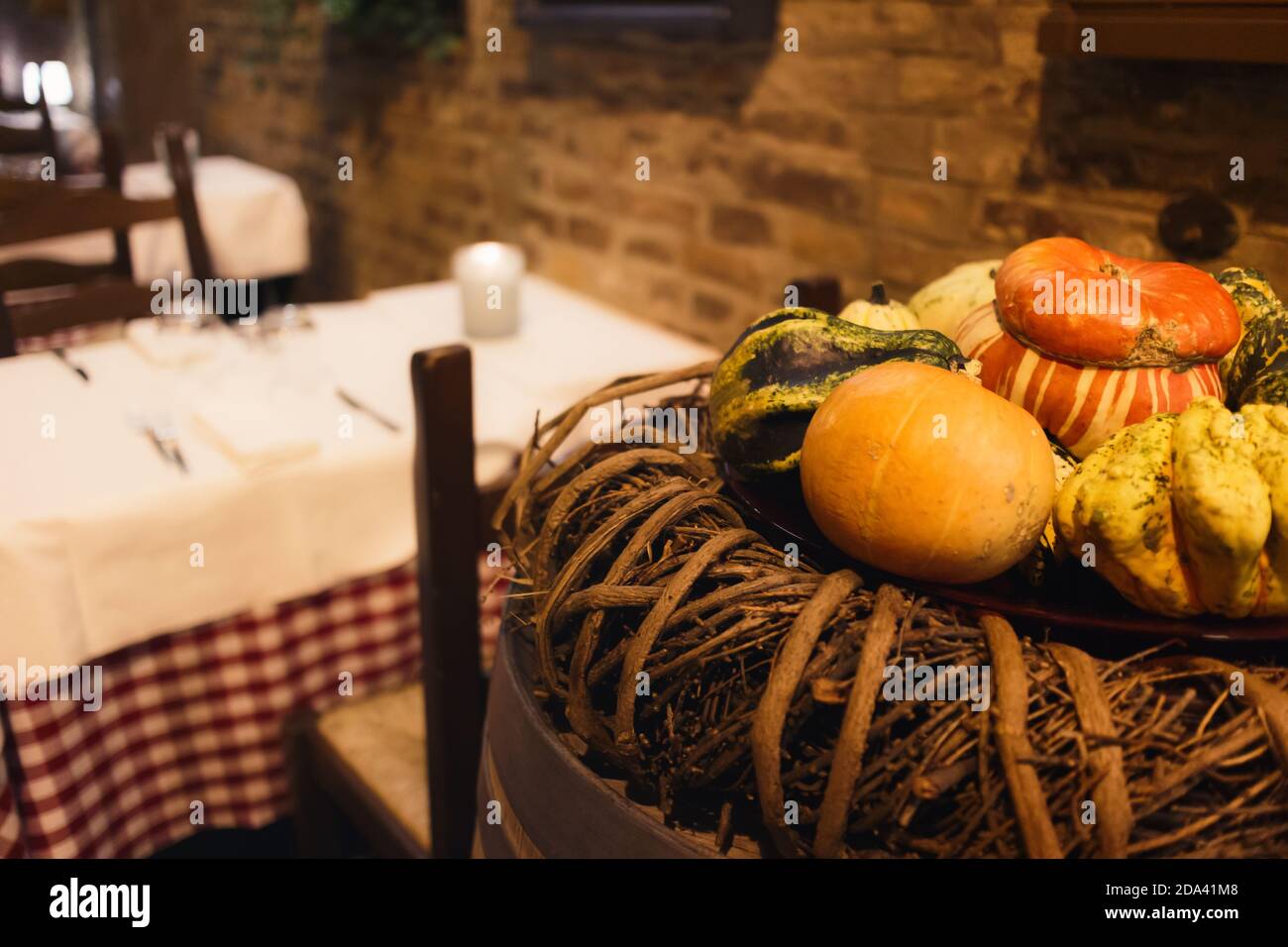 zucche decorative nella stagione autunnale vicino alle tabelle di un sala ristorante rustica italiana con tovaglie preparate Foto Stock