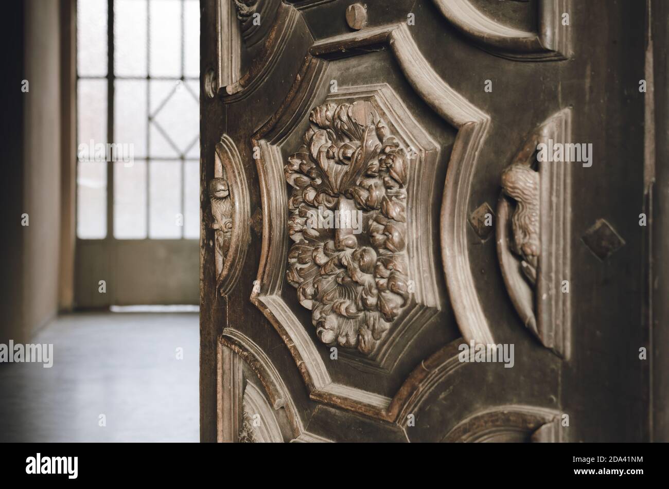 aprire la vecchia porta di casa in legno invecchiata con decorazioni a forma di faccia e stanza illuminata sullo sfondo Foto Stock