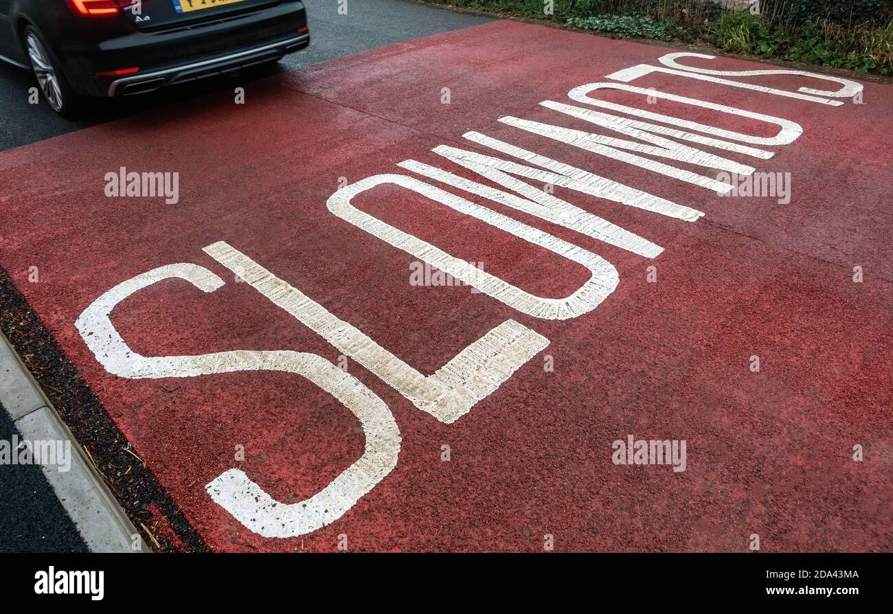 segno lento scritto sulla strada con auto di passaggio Foto Stock