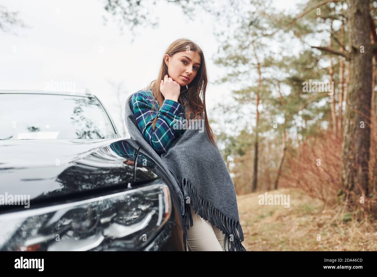 Giovane ragazza allegra in piedi vicino a una moderna auto nera all'aperto la foresta Foto Stock