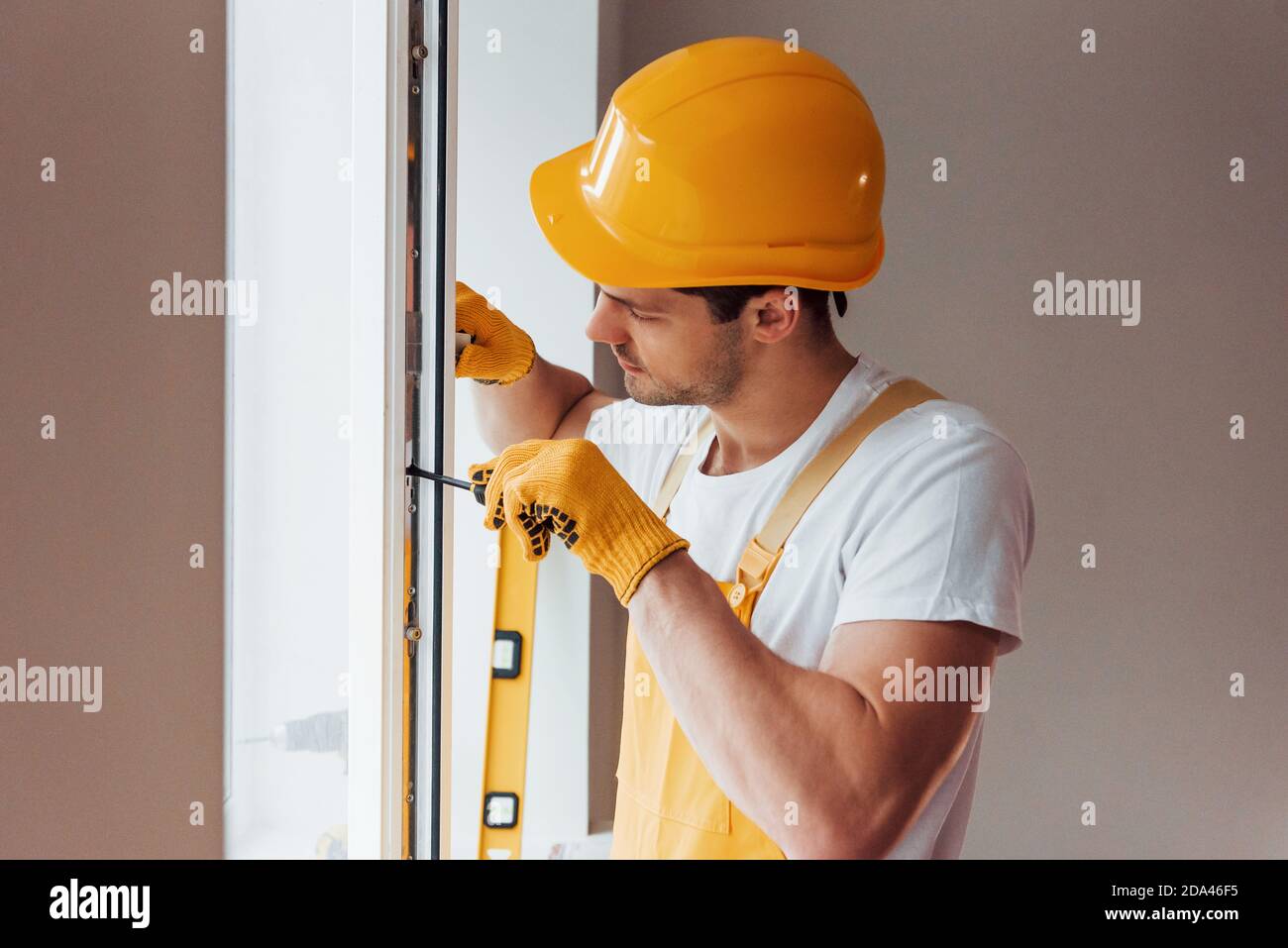 Handyman in uniforme gialla installa una nuova finestra. Ristrutturazione casa concezione Foto Stock