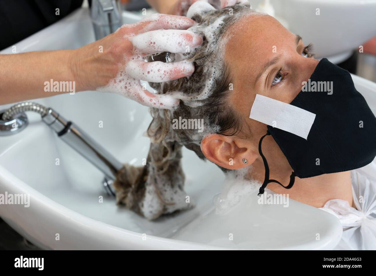 Donna parrucchiere mano lavaggio giovane donna cliente capelli in parrucchiere. Bella cliente che indossa maschera medica, pandemia coronavirus, nuova norma Foto Stock