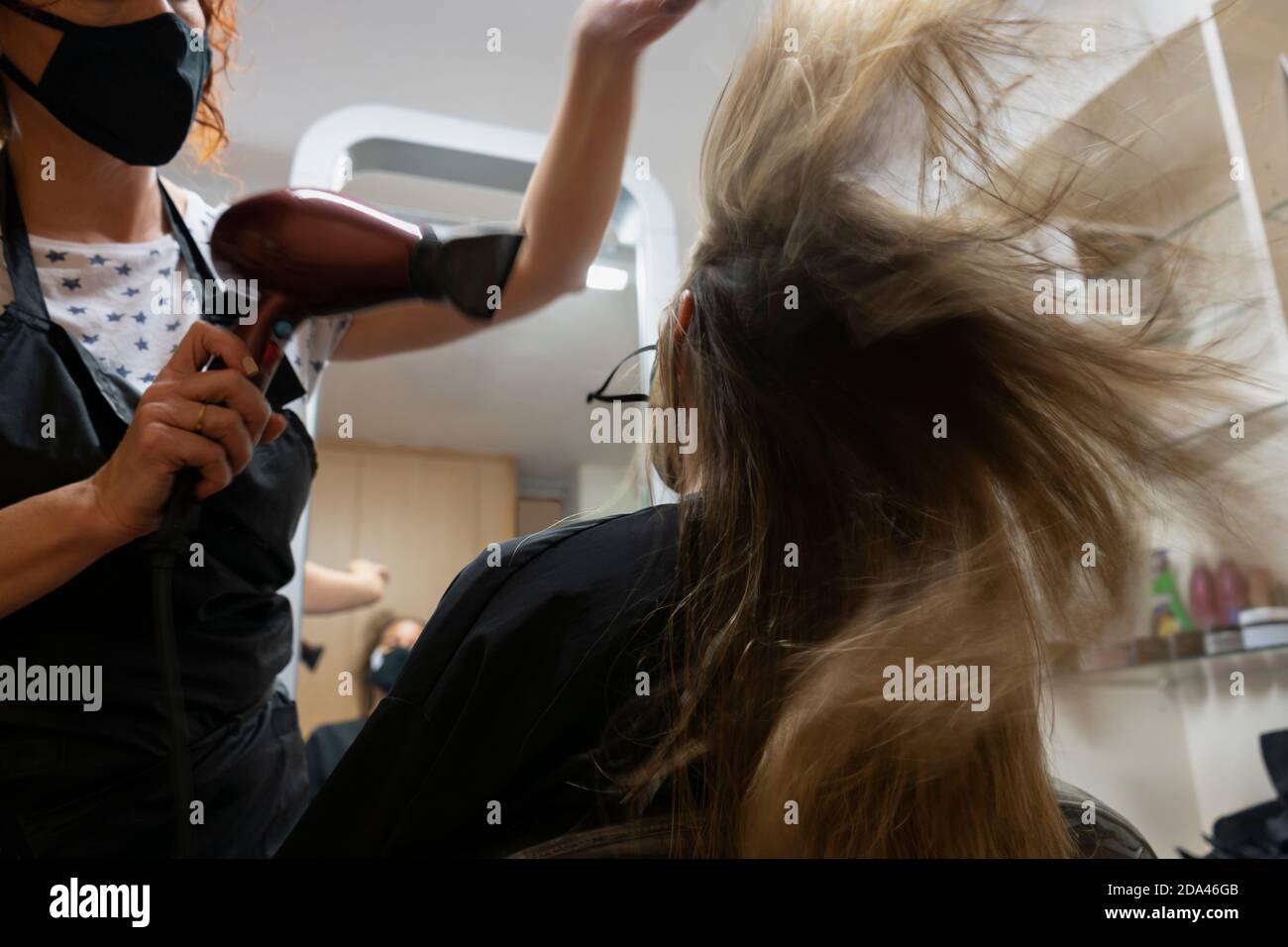 Professionale parrucchiere, stilista che fa acconciatura, asciugando e soffiando i capelli con un asciugacapelli in beauty salon.Hair care concept.wearing maschera medica, m Foto Stock