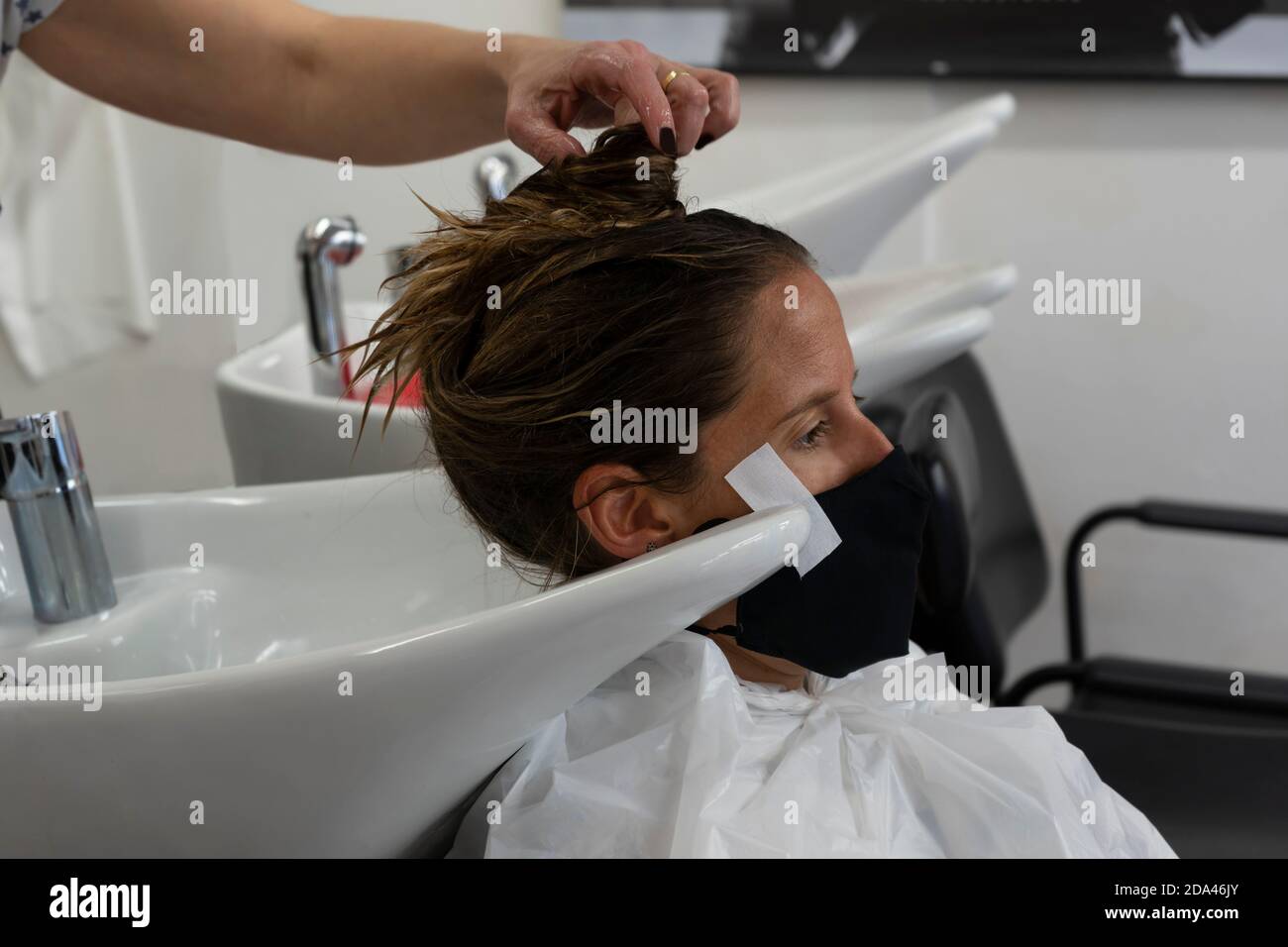 Donna parrucchiere mano lavaggio giovane donna cliente capelli in parrucchiere. Bella cliente che indossa maschera medica, pandemia coronavirus, nuova norma Foto Stock