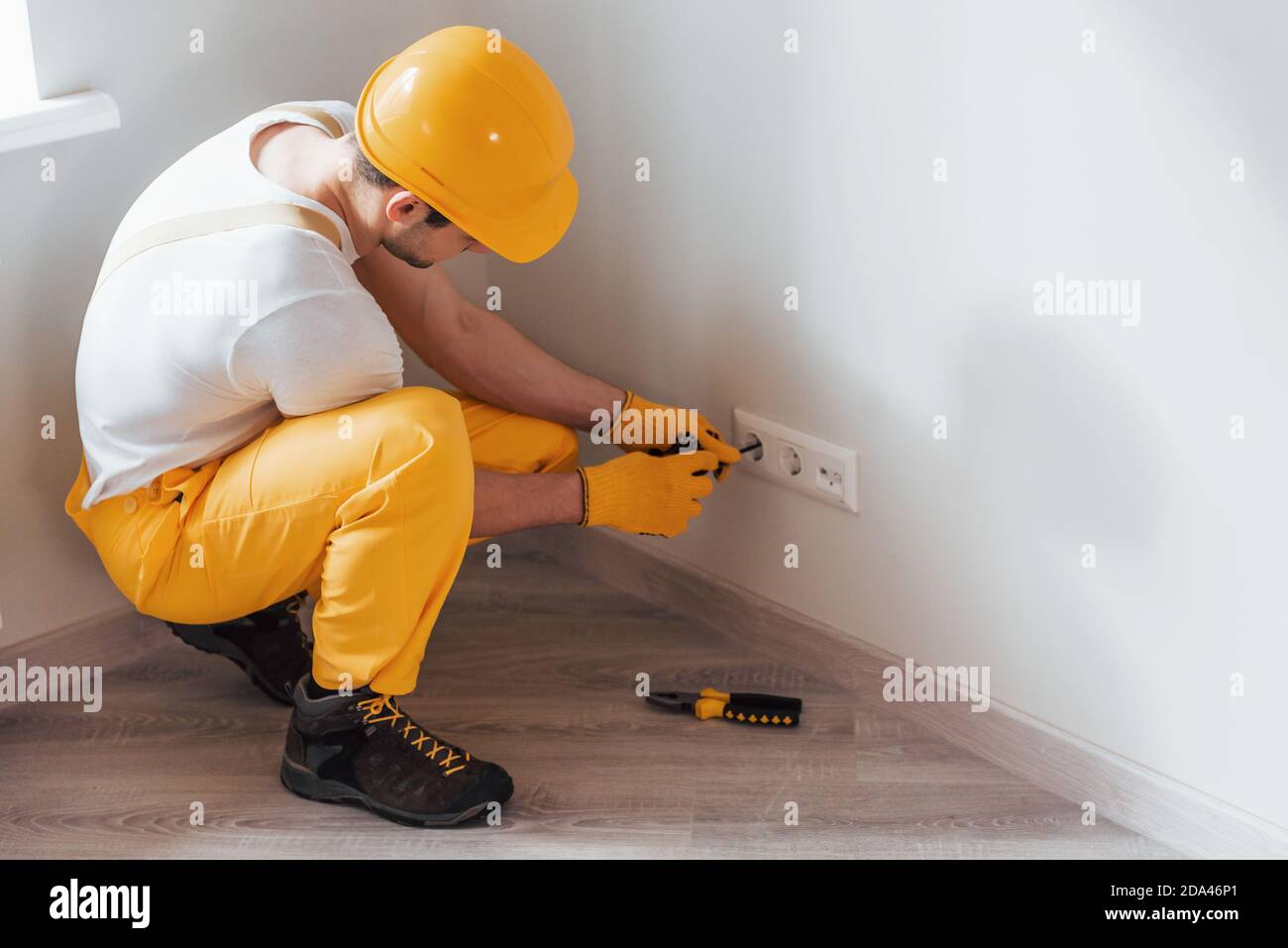 Handyman in uniforme gialla lavora con l'elettricità e l'installazione di una nuova presa. Ristrutturazione casa concezione Foto Stock