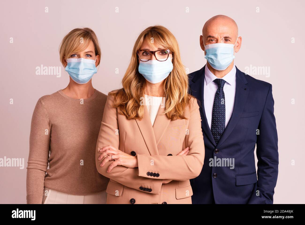 Gruppo di uomini d'affari che indossano maschere per il viso e guardano la fotocamera mentre si levano in piedi insieme su sfondo isolato. Foto Stock