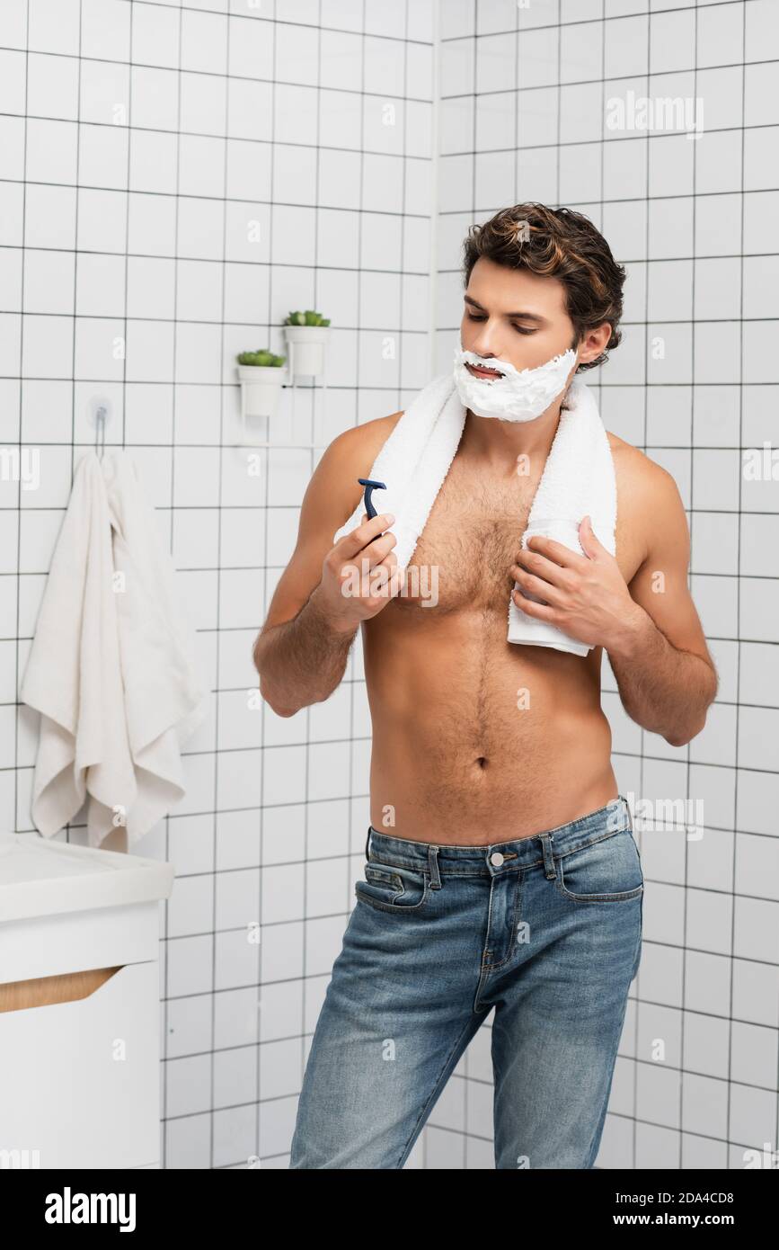 Uomo senza peli in jeans con schiuma da barba sulla presa del viso  asciugamano e rasoio in bagno Foto stock - Alamy