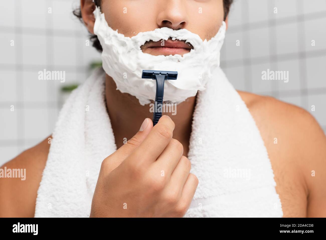 Vista tagliata del giovane uomo con schiuma da barba sul viso e asciugamano  intorno al collo che tiene il rasoio Foto stock - Alamy