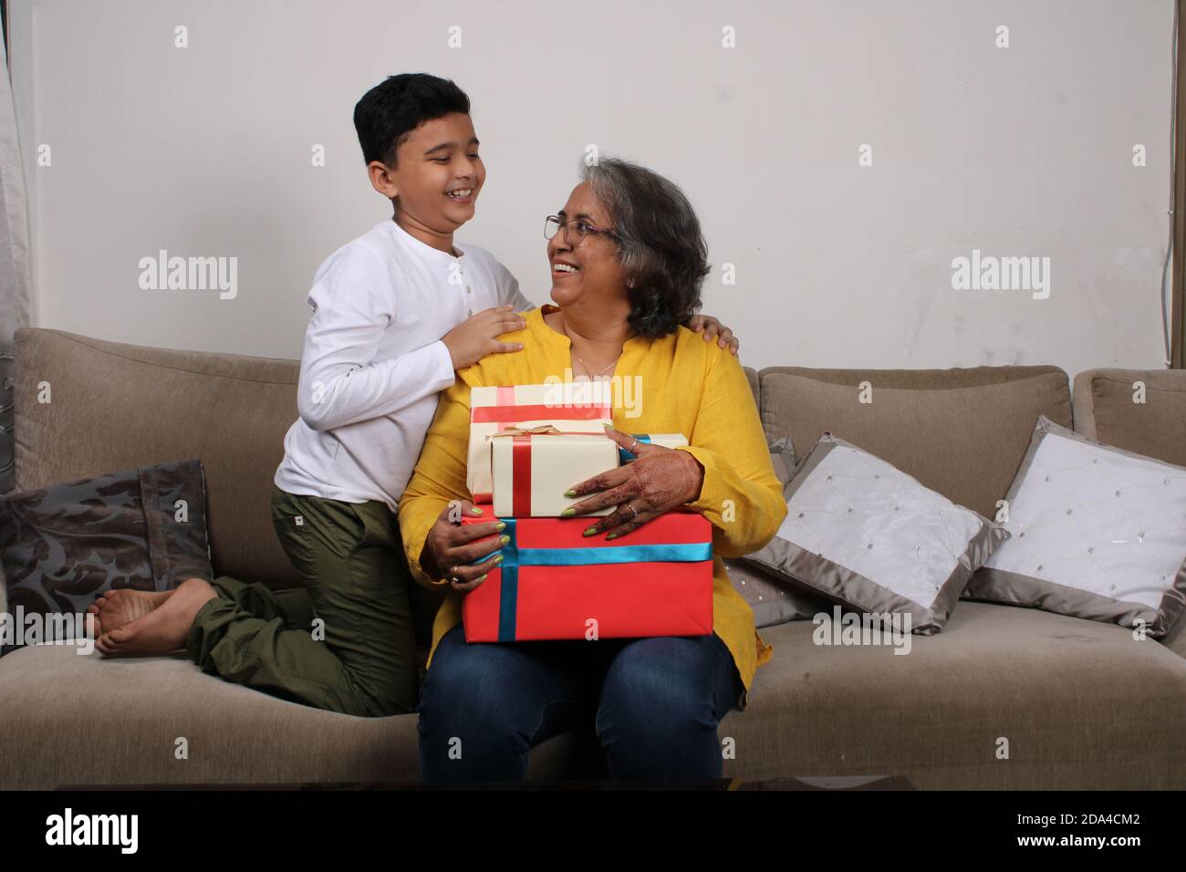 Allegro capretto indiano e sua madre grande seduta sul divano con i regali. Foto Stock