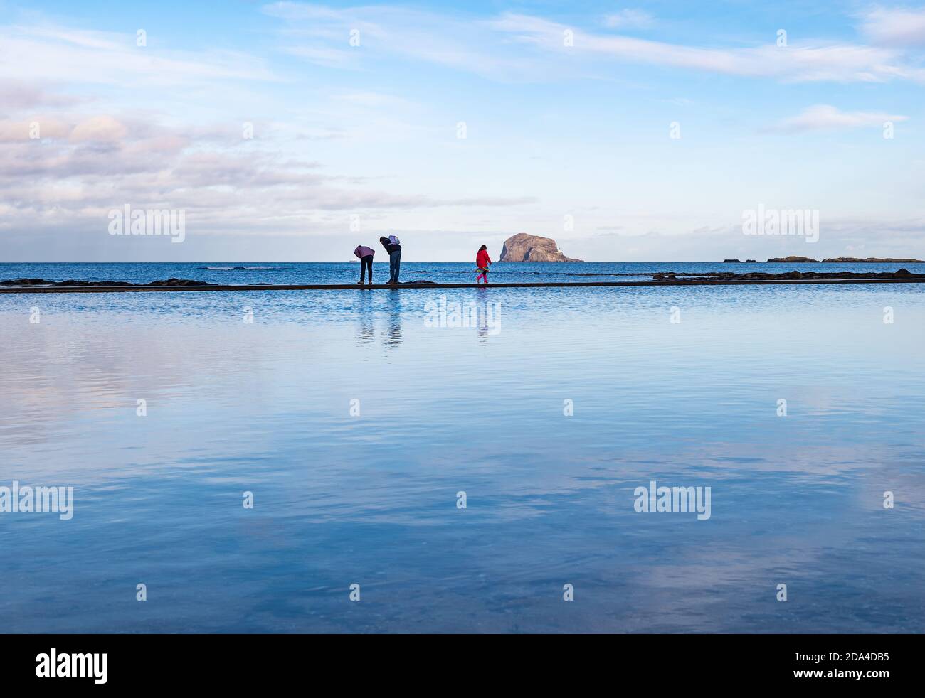 Peopl Ewalking sul bordo della piscina con Bass Rock all'orizzonte in giornata tranquilla, Milsey Bay, North Berwick, East Lothian, Scozia, Regno Unito Foto Stock