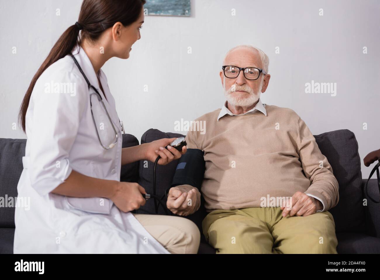 infermiere geriatrico brunette che esamina l'uomo anziano con stetoscopio Foto Stock