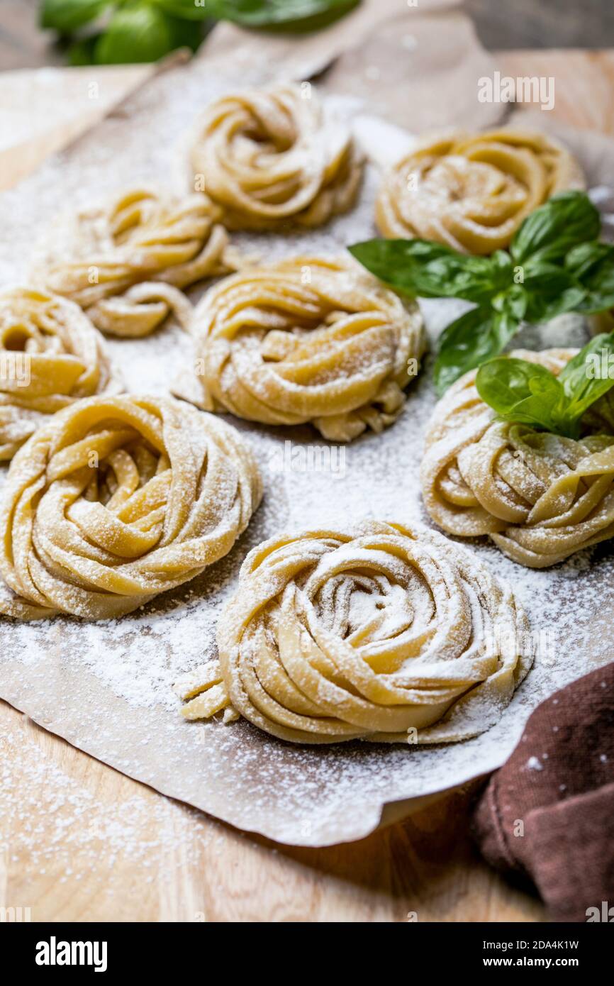 Pasta alluovo, Tagliatelle o fettuccine. Palline rotonde di pasta cruda sul tagliere di legno su sfondo nero Foto Stock