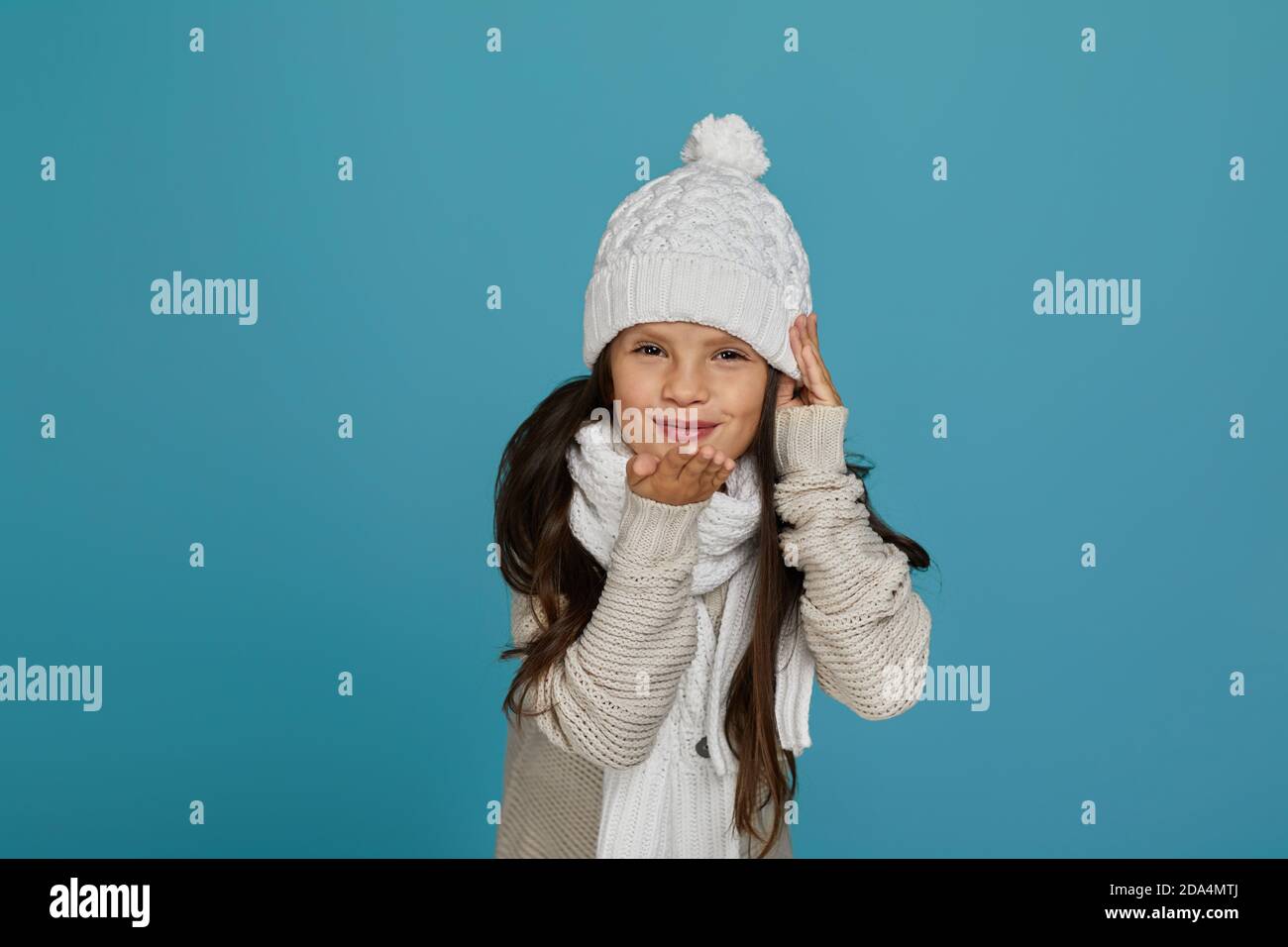ritratto di allegra bambina in cappello bianco invernale caldo e invio di  sciarpa soffiando un bacio aria isolato su blu sfondo Foto stock - Alamy