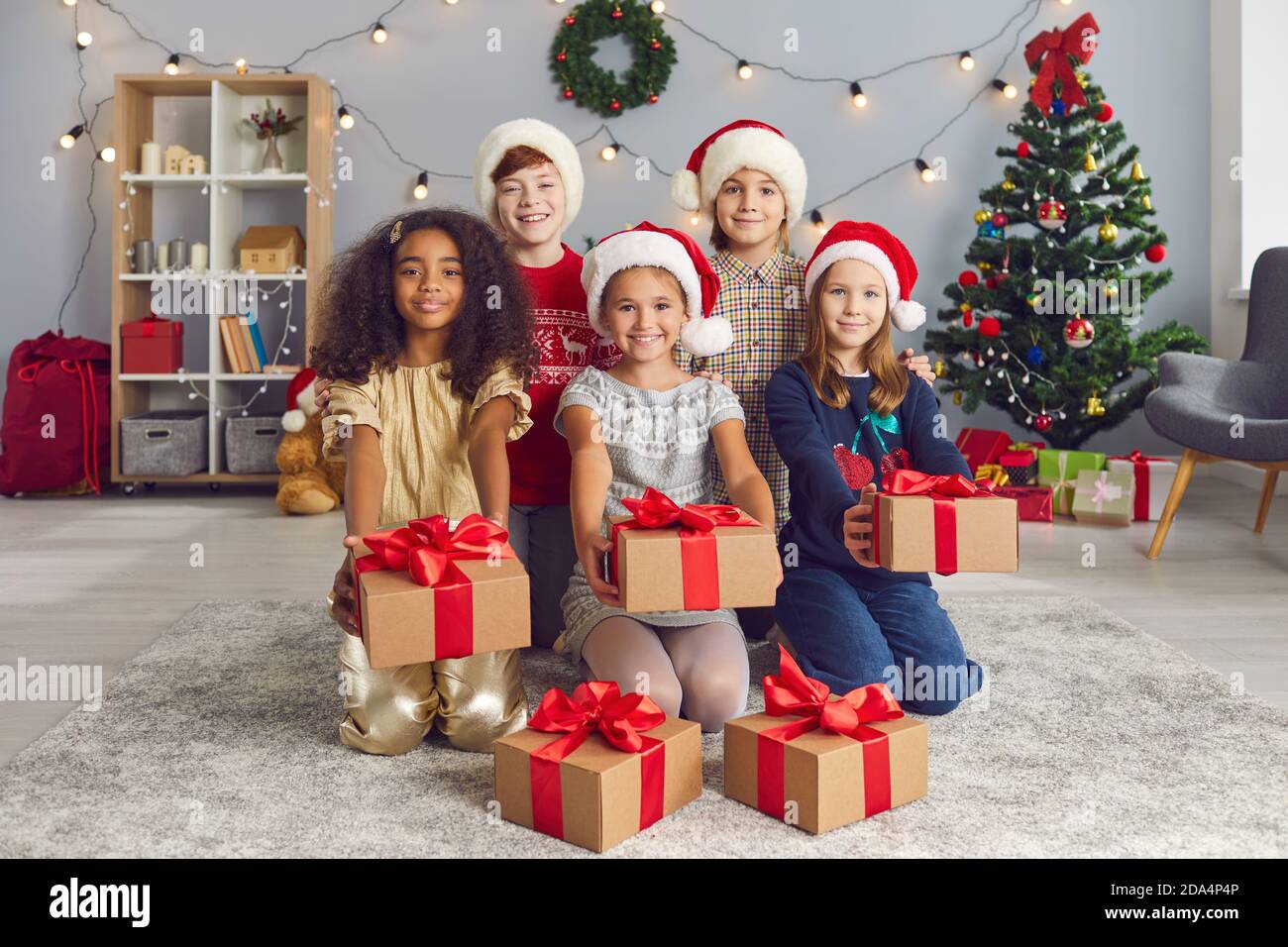 Gruppo di bambini sorridenti che tengono fuori le scatole di regalo di Natale legato con nastri rossi Foto Stock