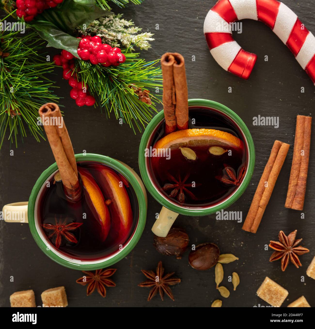 VIN brulé, bevanda alcolica invernale, due tazze d'epoca, ingredienti arancio e spezie e decorazioni natalizie su pietra nera, vista dall'alto. Foto Stock