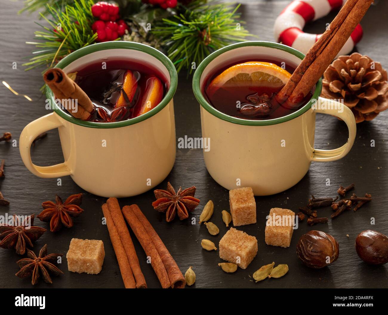 VIN brulé, bevanda alcolica invernale calda, due tazze d'epoca, ingredienti arancio e spezie e decorazioni natalizie su pietra nera, vista closeup. Foto Stock