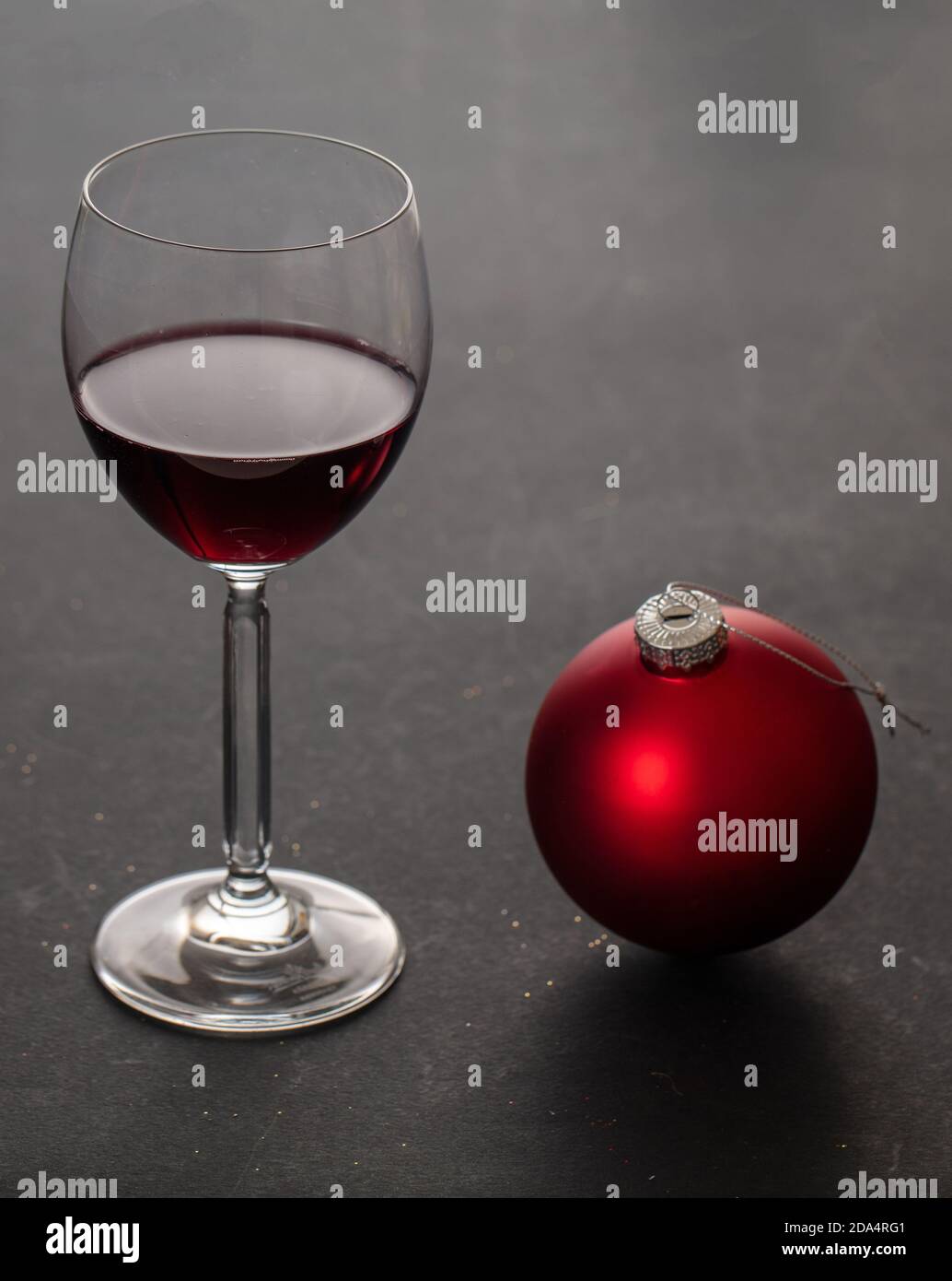 Vino rosso di Natale. Wineglass e rosso xmas ornamento bauble, sfondo nero, closeup vista verticale. Festa invernale Foto Stock