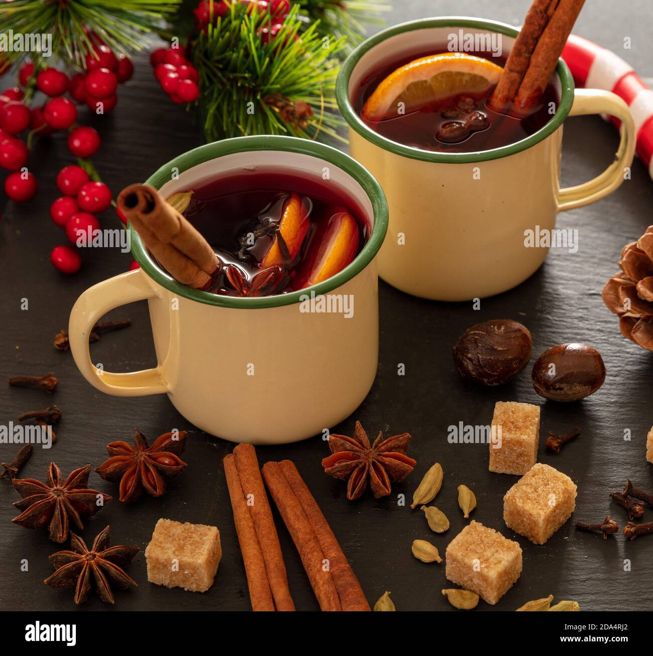 VIN brulé, bevanda alcolica invernale calda, due tazze d'epoca, ingredienti arancio e spezie e decorazioni natalizie su pietra nera, vista closeup. Foto Stock