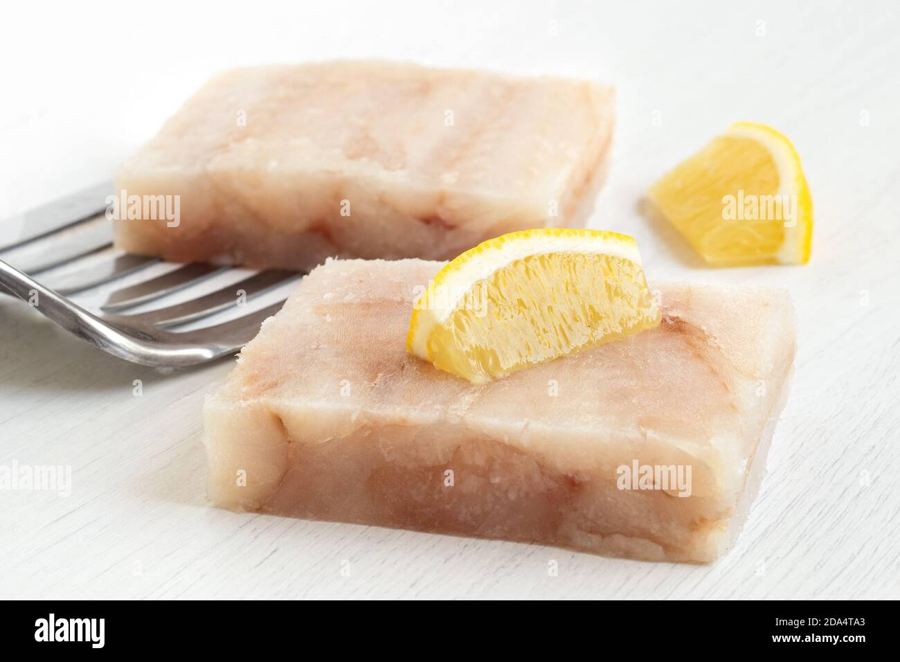 Due filetti di pesce surgelati con spicchi di limone e spatola in metallo su bianco. Foto Stock