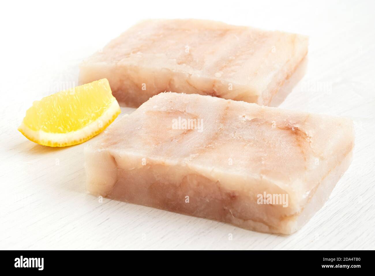 Due blocchi di filetto di pollock surgelati con un cuneo di limone isolato su bianco. Foto Stock