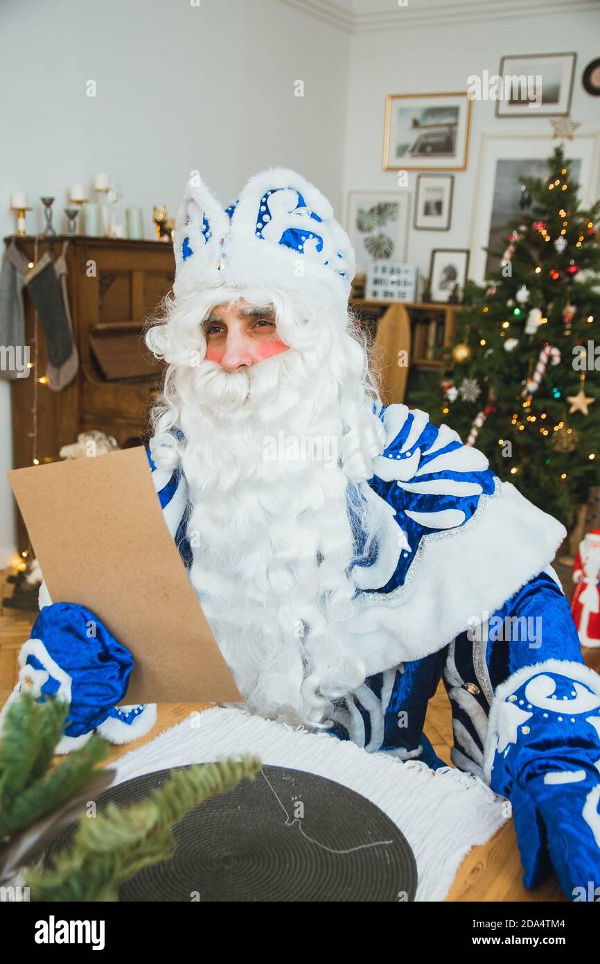 Babbo Natale in un cappotto di pelliccia blu legge una lettera da un bambino sullo sfondo di un albero di Natale. Foto Stock