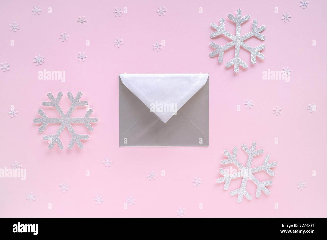 Busta argento con biglietto d'auguri e fiocchi di neve su sfondo rosa pastello. Lettera con congratulazioni, lettera a Babbo Natale. Natale o Capodanno Foto Stock