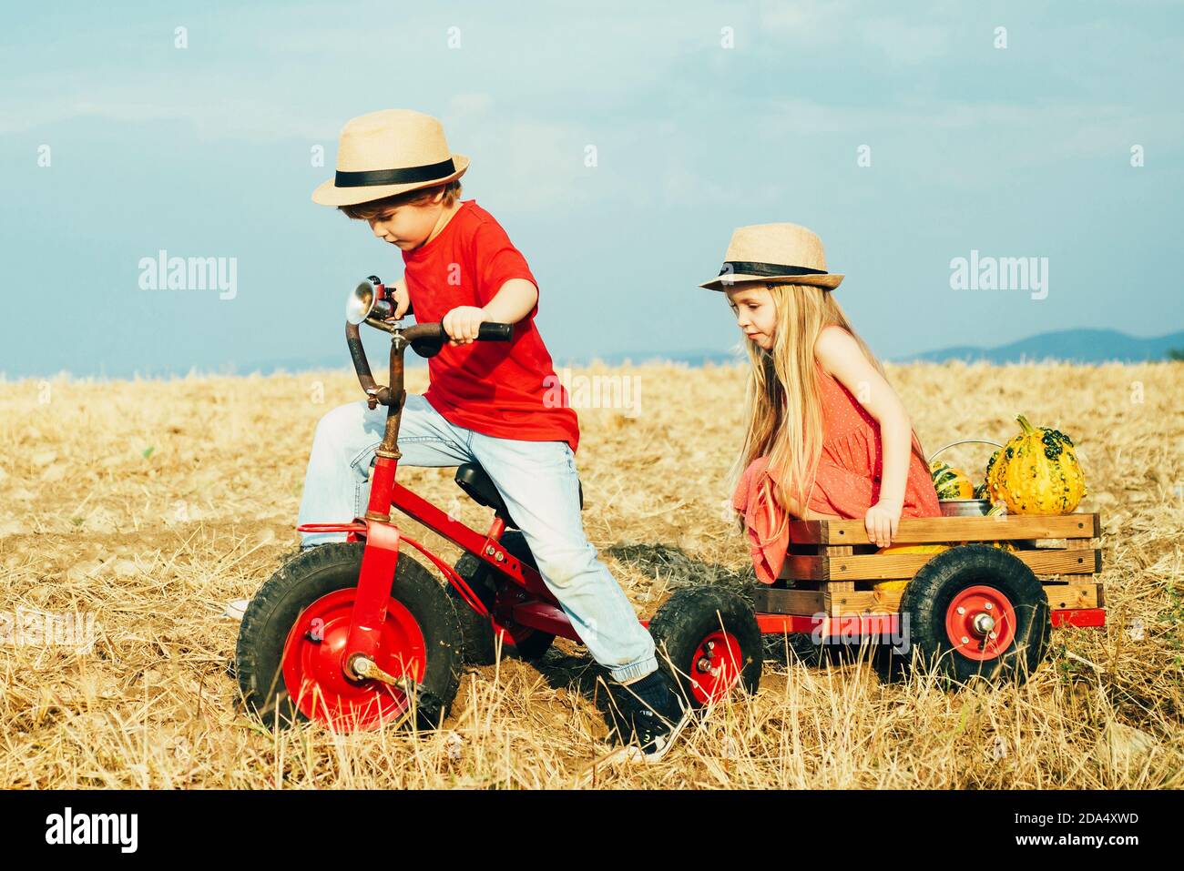 Bambini che giocano e si pedalano all'aperto. Due bambini che si divertono sul campo contro lo sfondo blu del cielo. Giorno della terra. Fattoria ecologica. Due giovani agricoltori Foto Stock