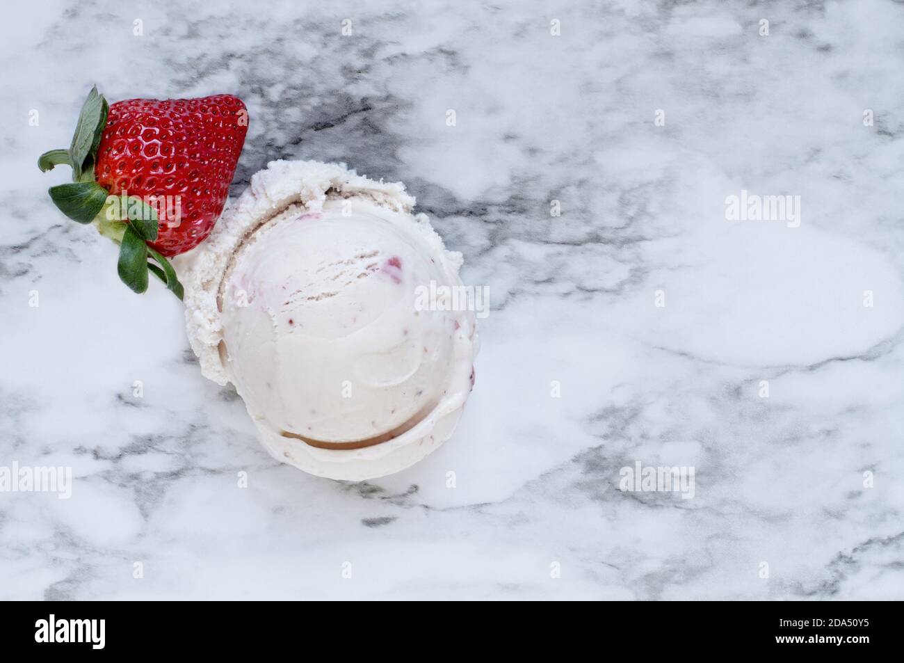 Vista su un piatto di gelato alla fragola rosa con una sola frutta fresca alla fragola su uno sfondo di marmo bianco e grigio. Vista dall'alto. Foto Stock