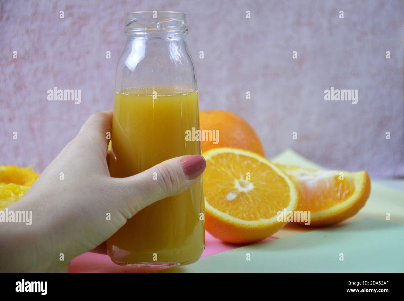 Mano donna con succo d'arancia appena spremuto in una bottiglia e orandes su sfondo a colori Foto Stock