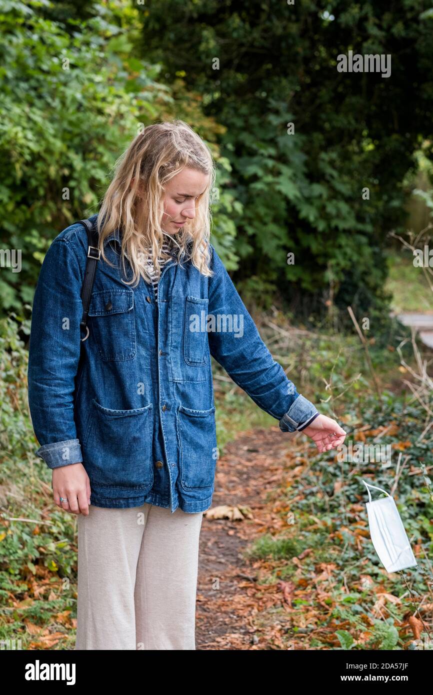 Giovane bionda donna in piedi in foresta, gettando via maschera chirurgica viso. Foto Stock