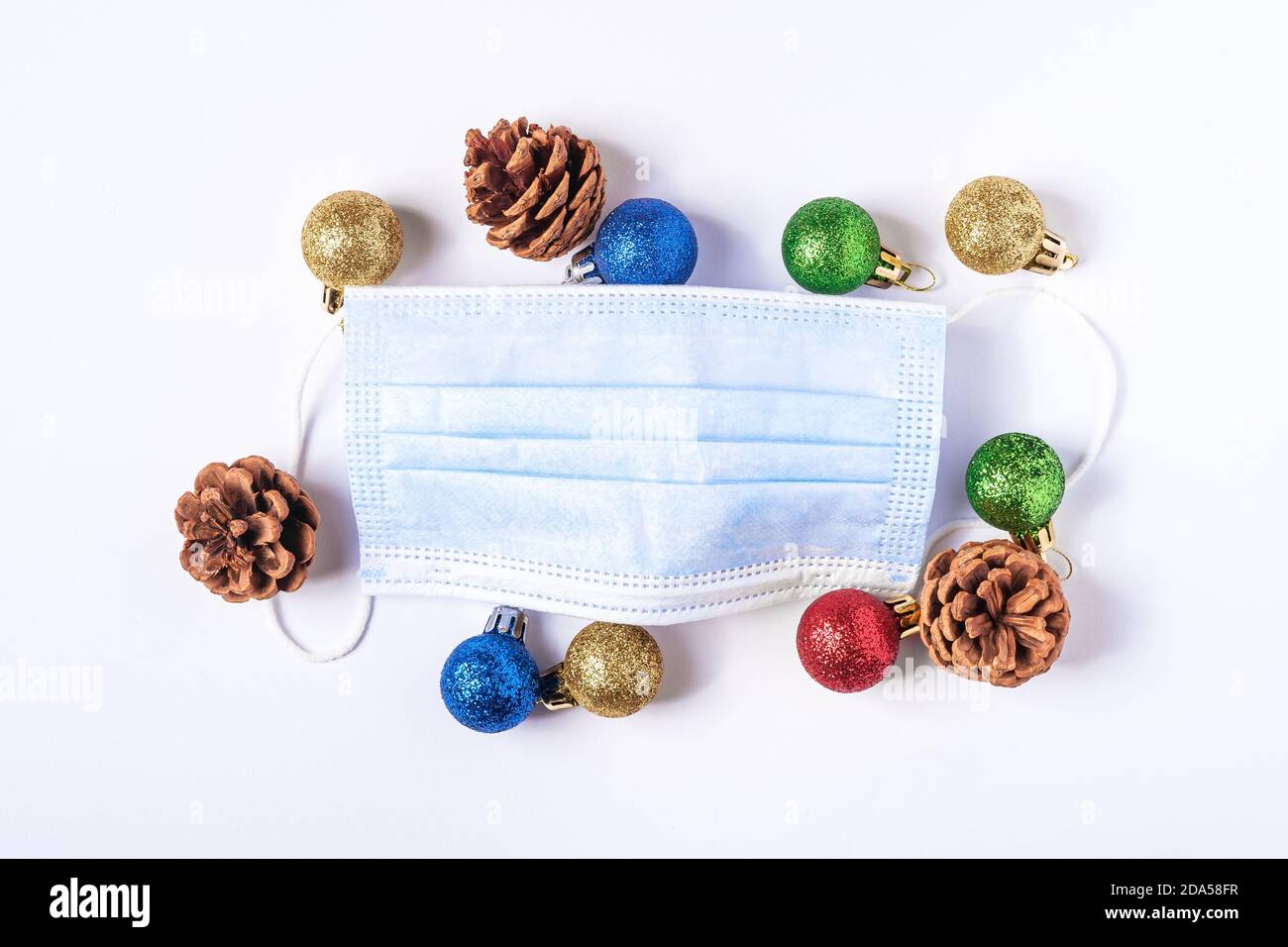 Composizione natalizia con maschera medica e palline colorate, decorazioni ornamentali su sfondo bianco Foto Stock