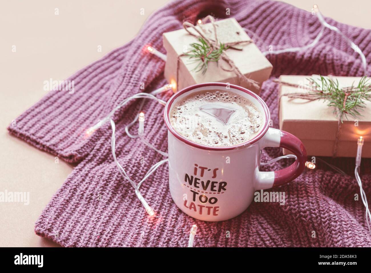 Una tazza di bevanda calda con schiuma e due scatole di regali su un maglione a maglia, decorato con un ghirland Foto Stock