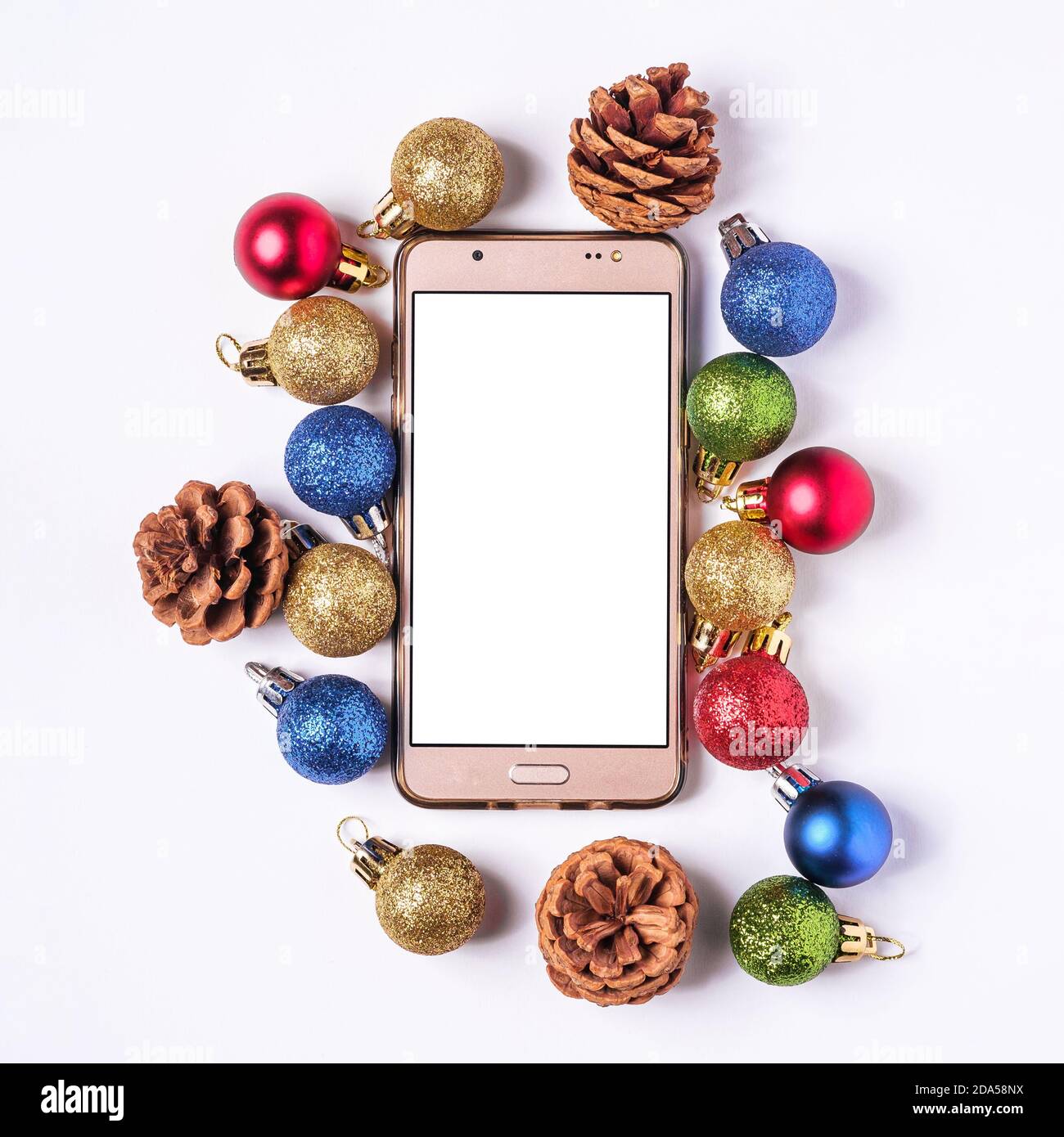 Shopping online di Natale. Mokup smartphone con schermo bianco vuoto. Palline colorate e decorazioni con coni di pino. Foto Stock