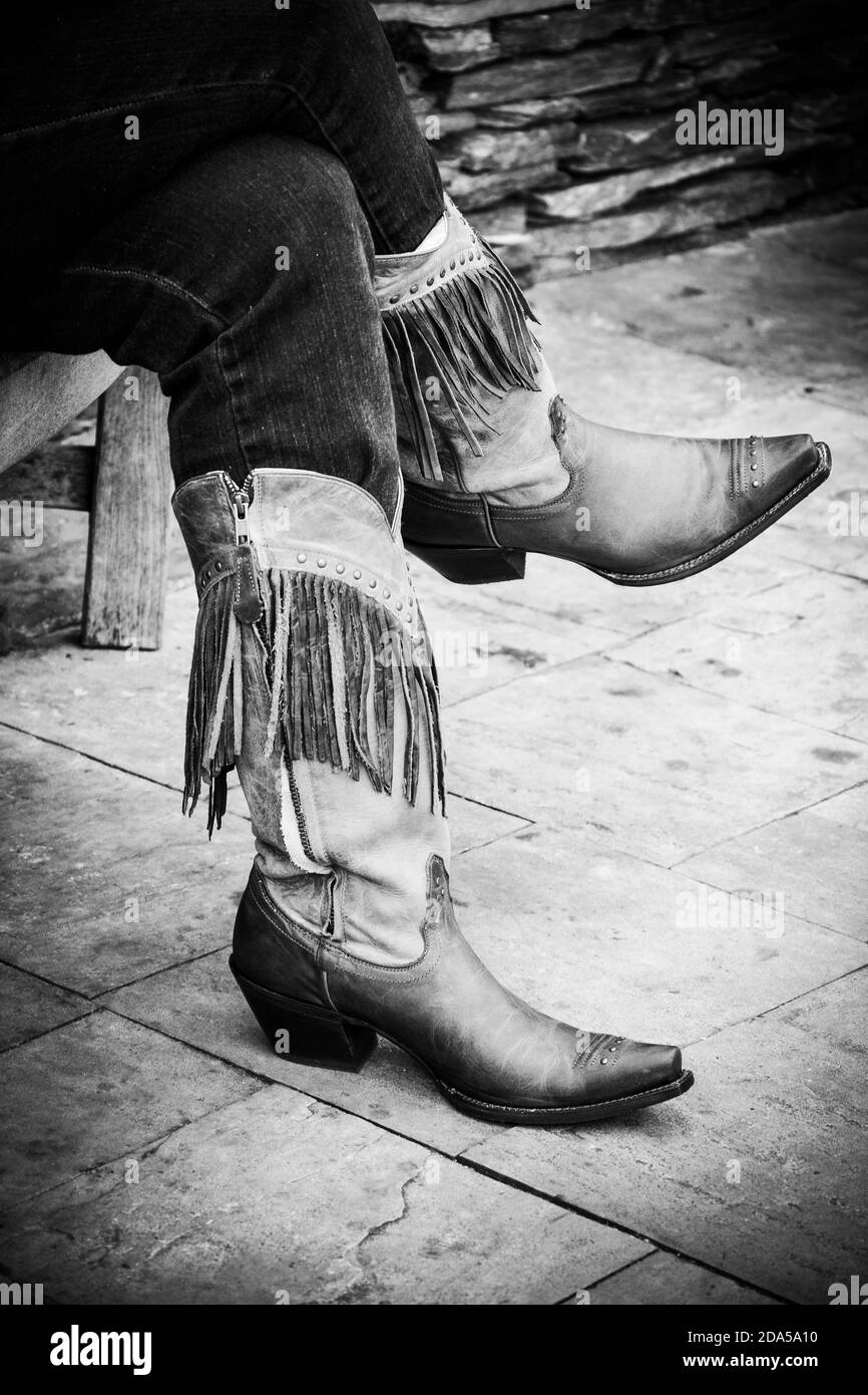 Primo piano di gambe incrociate in jeans rimboccati all'interno stivali da cowgirl con frange sul marciapiede in bianco e nero Stati Uniti meridionali Foto Stock