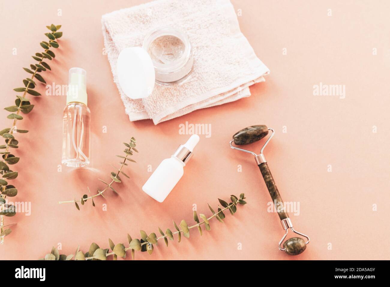 Cosmetici naturali. Tonico viso e siero in bottiglie senza marchio, vasetto crema, rullo massaggiante, asciugamano e eucalipto Foto Stock