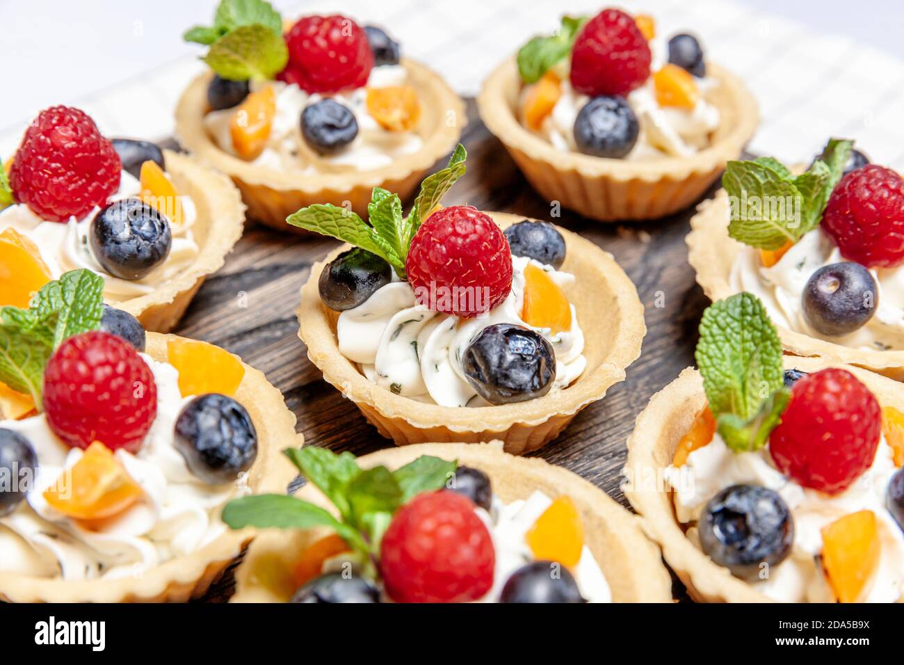 Dessert con tartine di frutta e frutti di bosco assortito su vassoio di  legno. Clooseup di deliziosi dolci pasticceria torte torte colorate con  lampone naturale fresco di mirtillo e crema di formaggio.