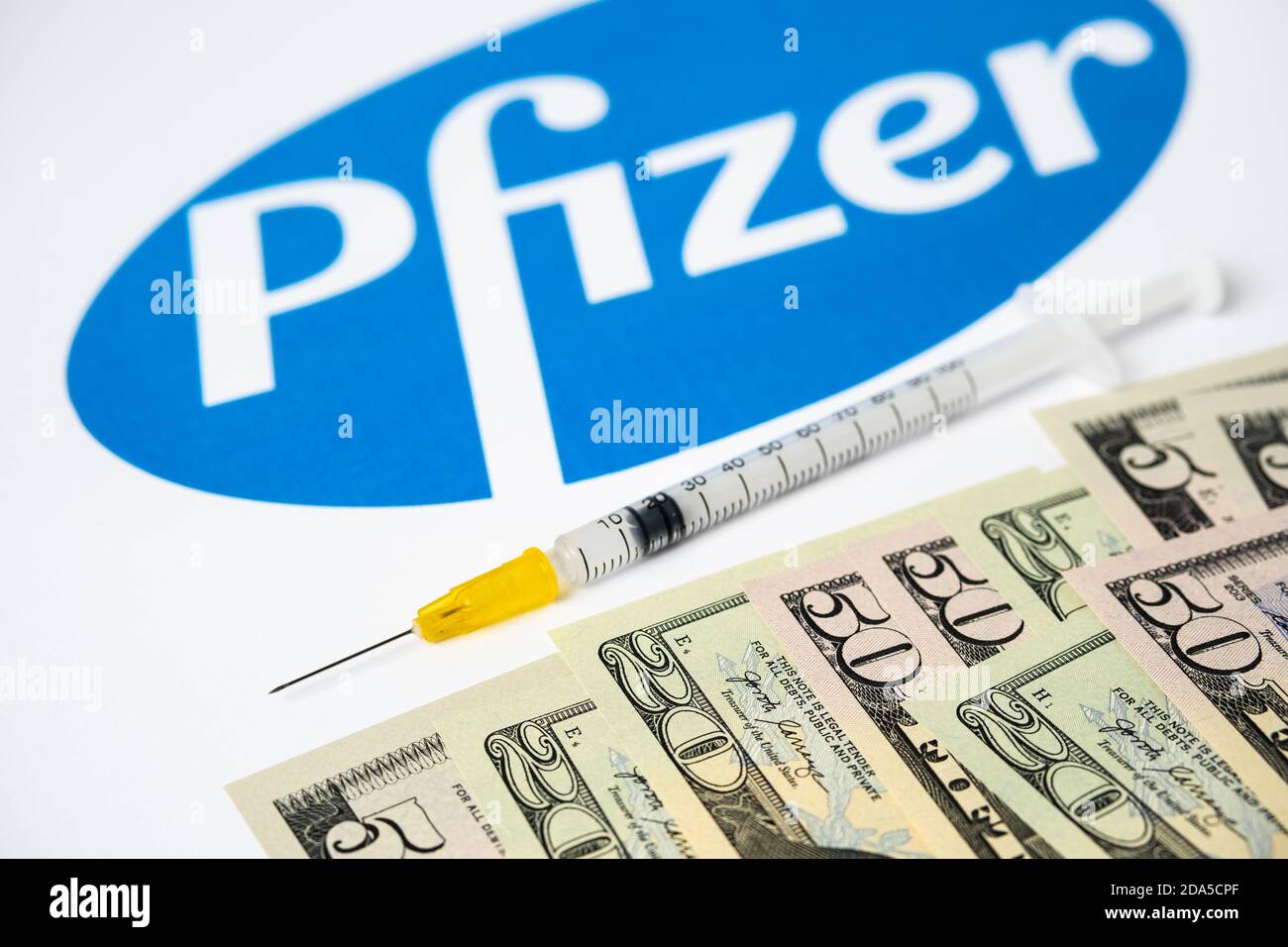 Stafford / Regno Unito - 9 novembre 2020: Concetto di vaccino Pfizer Covid-19. Siringa bilanciata sulla punta di un dito e logo aziendale di Pfizer sfocato sulla b Foto Stock