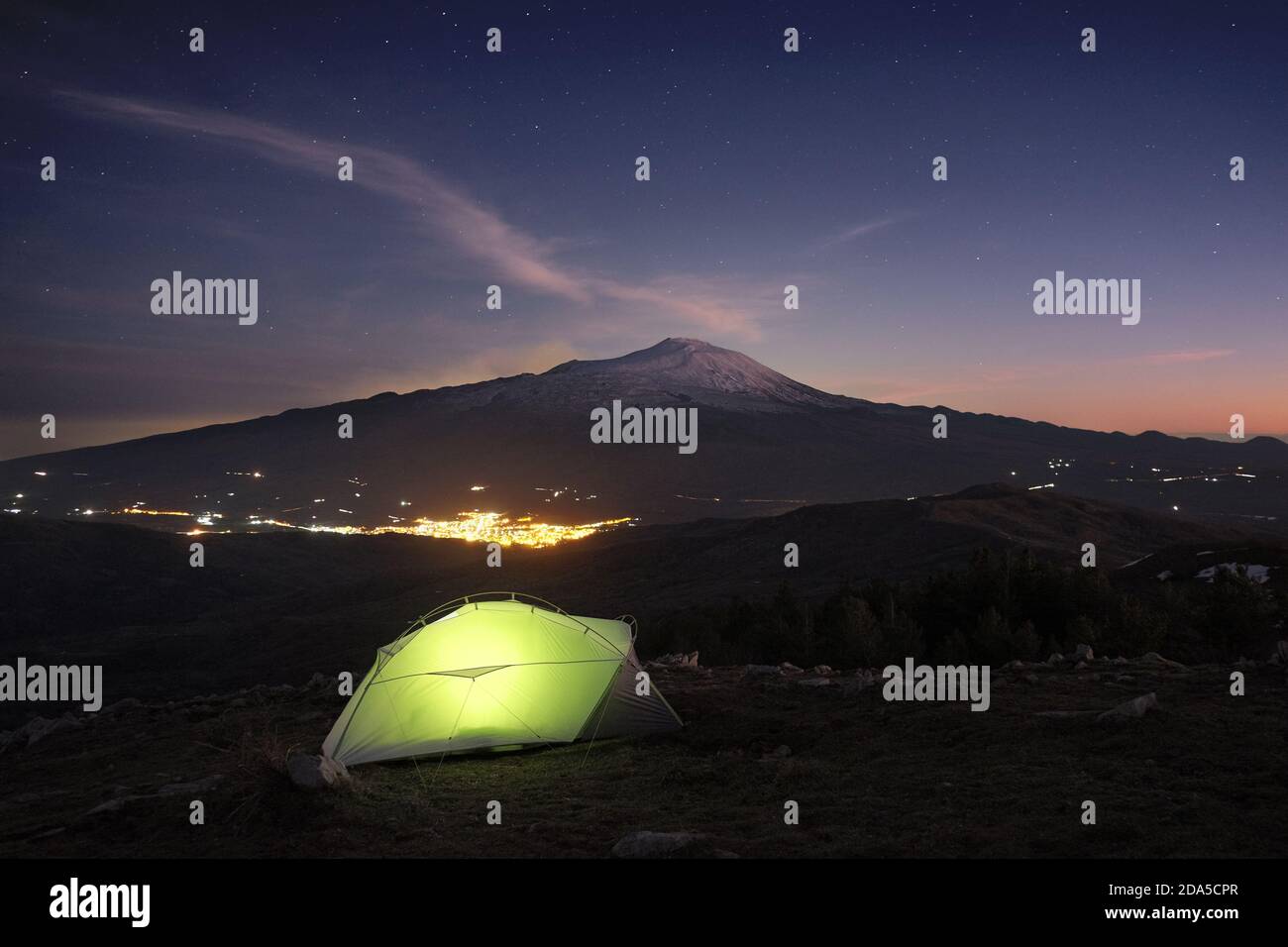 Tenda illuminata sulla montagna del Parco dei Nebrodi al crepuscolo, su luci di fondo della città sotto il vulcano Etna e cielo stellato, Sicilia Foto Stock