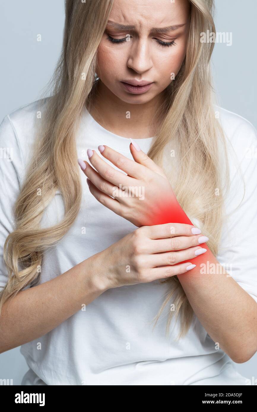 Giovane donna caucasica che tiene il suo polso doloroso causato da un lavoro prolungato sul computer, computer portatile. Sindrome del tunnel carpale, artrite, malattia neurologica Foto Stock