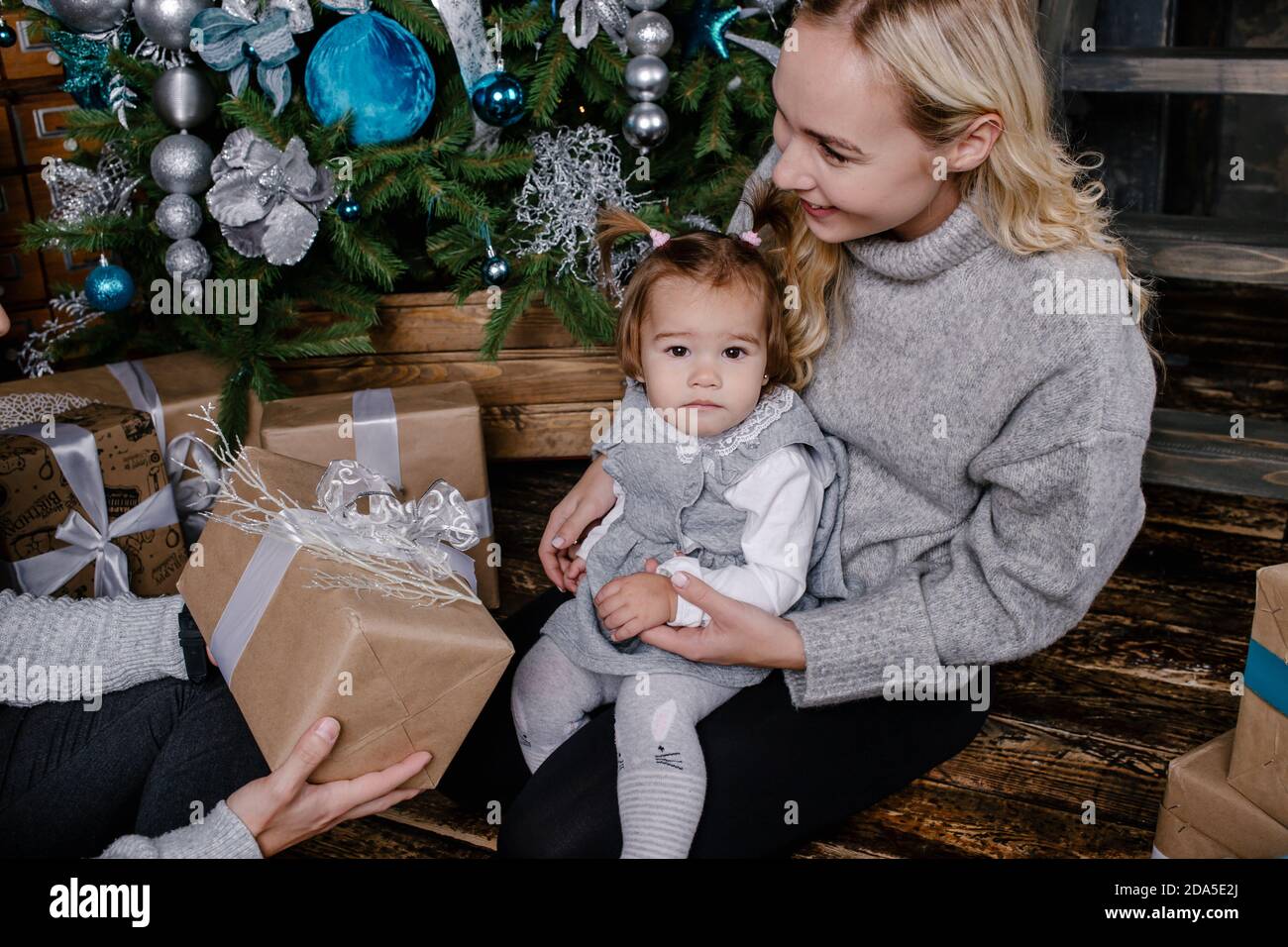 I genitori felici danno un regalo di Natale ad un bambino davanti all'albero di Natale. Baby girl guarda la macchina fotografica. Vacanze, regali, natale, x-mas Foto Stock
