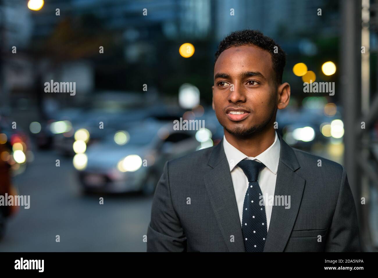 Bell'uomo d'affari africano all'aperto di notte sorridente e pensante Foto Stock