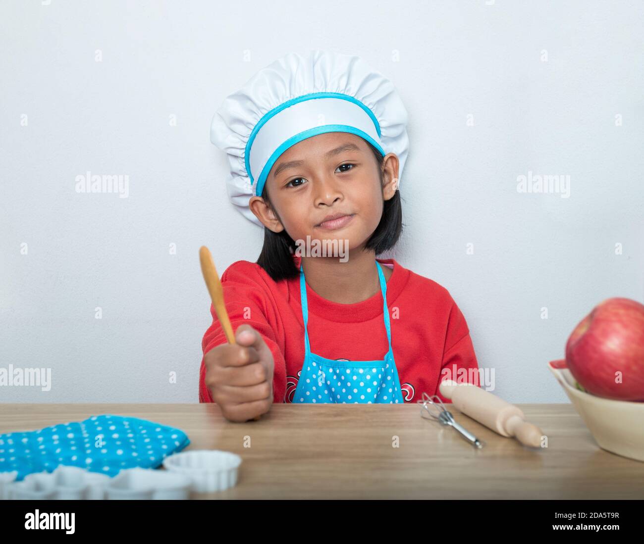 Ragazza carina in uniforme chef e simulati giocattoli di cucina nel banco della cucina. Foto Stock
