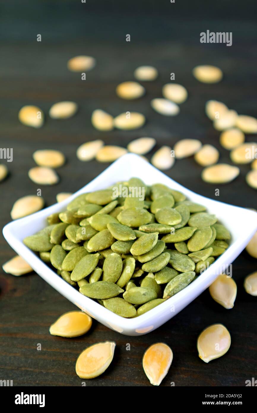 Immagine verticale di semi di zucca arrostiti con semi grezzi sparsi intorno su tavolo di legno Foto Stock