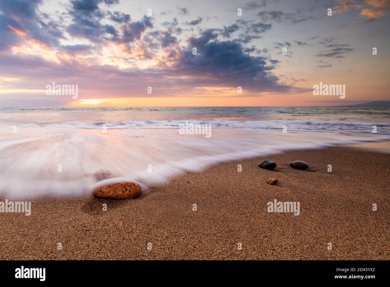 Un Rush of Wave Water arriva alla Shore AS Il sole si imposta sull'orizzonte dell'oceano Foto Stock