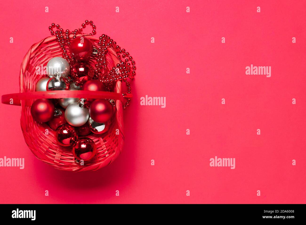 fock up di un cesto di vimini rosso con rosso e. Palline e perline d'argento sull'albero di Natale su uno sfondo vivace Foto Stock