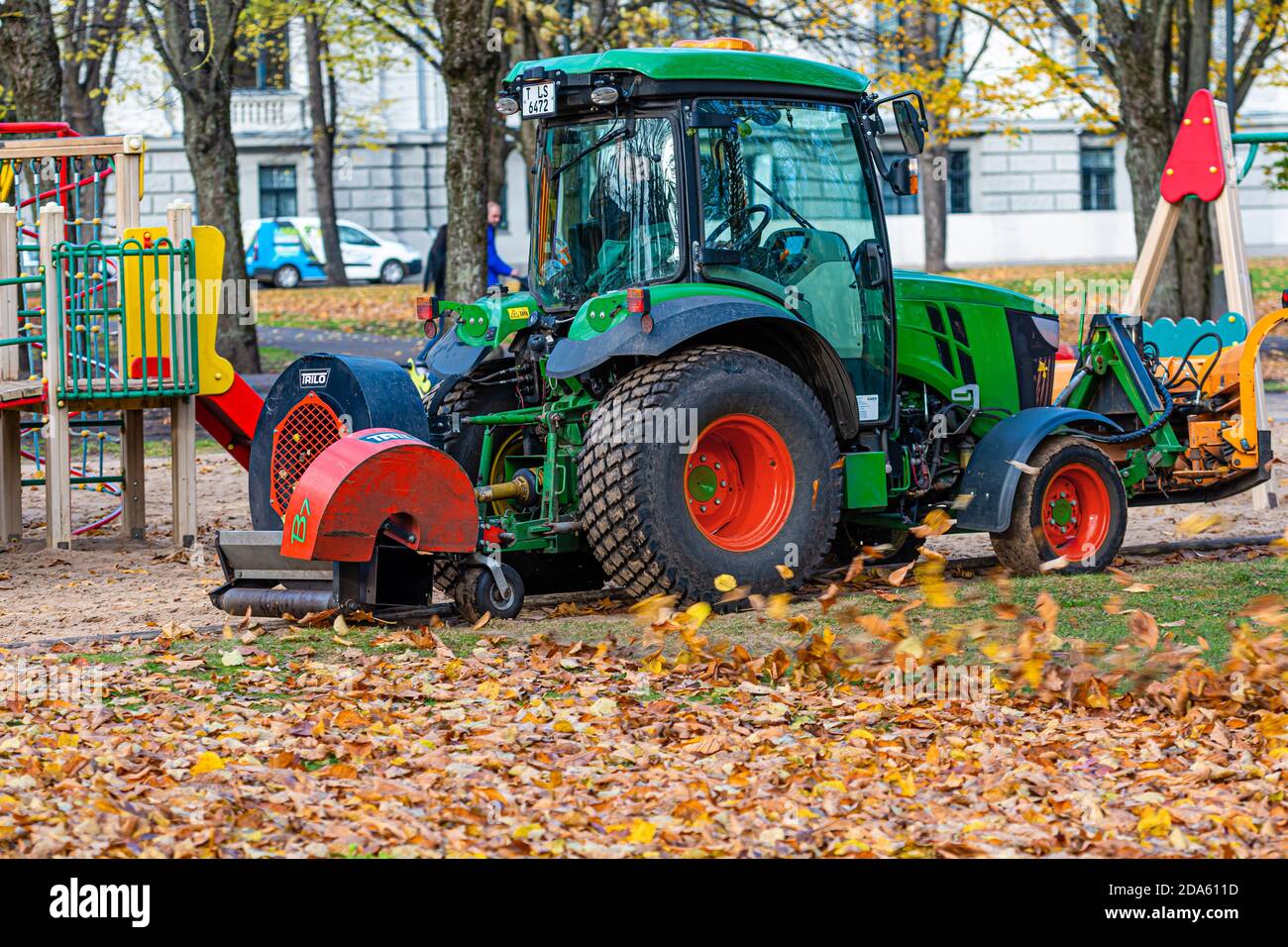 Riga, Lettonia - 6 novembre 2020: Un trattore con soffiatore pulisce un prato del parco cittadino e soffia via le foglie autunnali Foto Stock