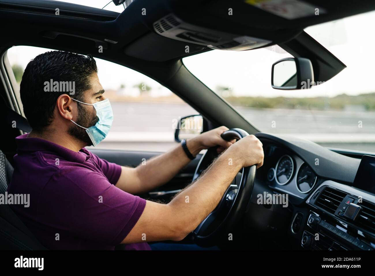 Uomo che guida un'auto indossando su una maschera medica durante Una pandemia di Covid-19 Foto Stock