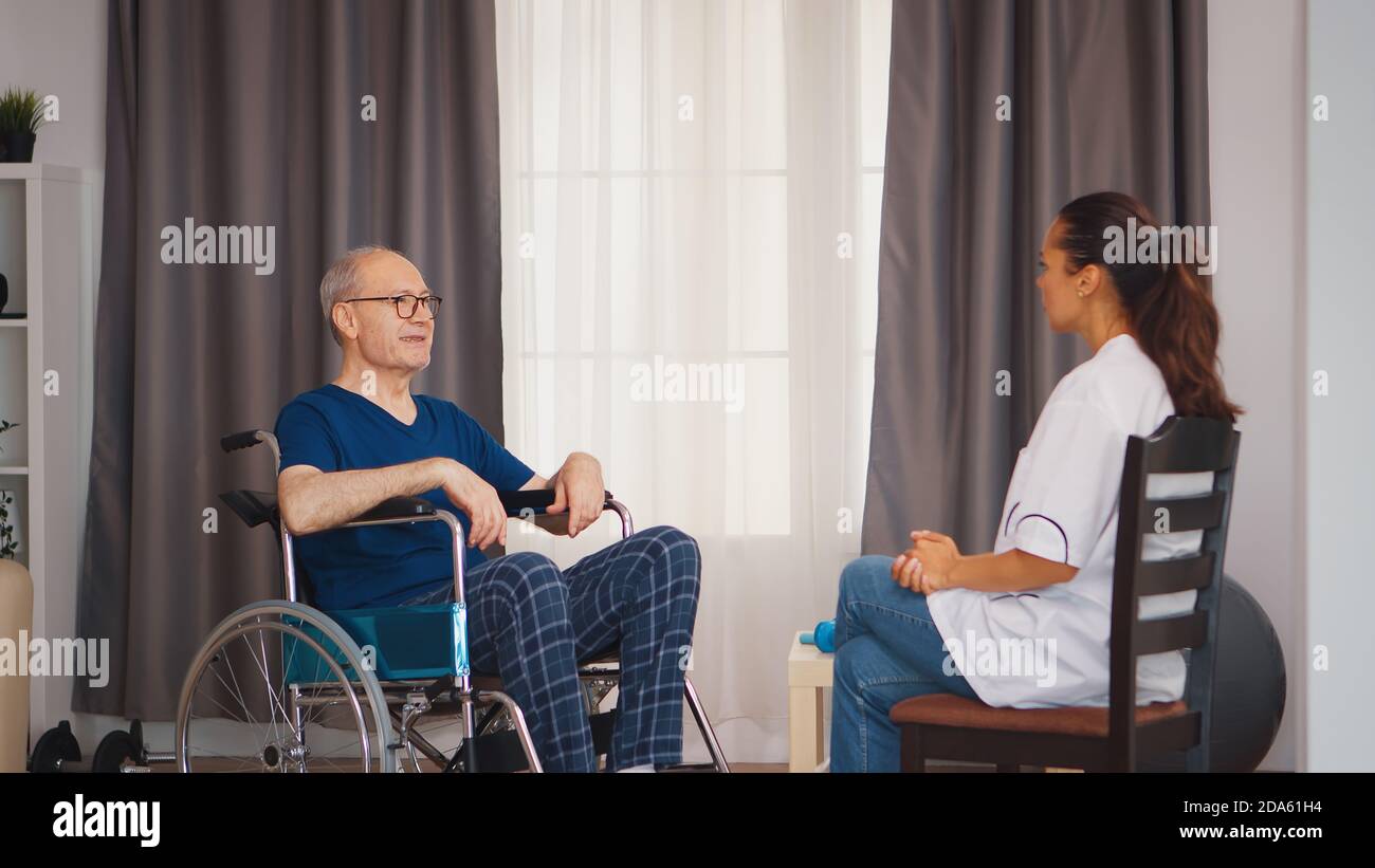 Anziano in sedia a rotelle che parla con il medico. Invalidità persona anziano con operatore medico in assistenza infermieristica a casa, assistenza sanitaria e medicina Foto Stock